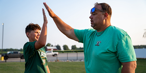 A football coach and young player giving a high five on a grass field during training